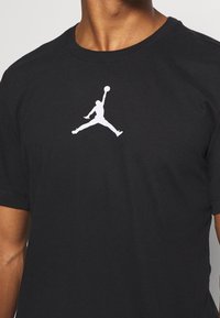 Svart bomulls-T-shirt med en stor vit Jordan-logotyp på bröstet. Designen inkluderar en rund halsringning och korta ärmar.