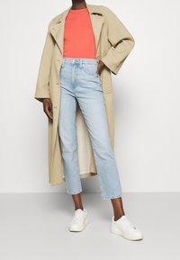 Beige long coat, coral shirt, light blue high-waisted jeans, and white sneakers. Smooth texture, relaxed fit, and cropped design.
