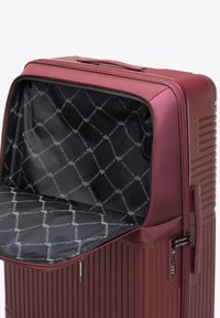 Valise rigide violette avec un extérieur strié, une fermeture éclair et un intérieur noir avec un motif de logo en répétition.