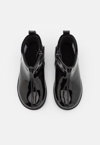 Botas de tobillo de charol negro con una superficie suave y brillante. Presentan cremalleras y un forro de tela negra suave. Diseño de punta redondeada.