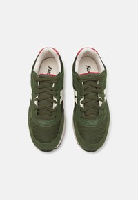 Green suede and mesh sneakers with white accents, dark laces, and a red-lined collar. Textured surface and round toe design.