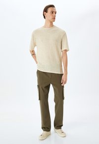 Beige gestreiftes Strickoberteil mit kurzen Ärmeln, kombiniert mit olivgrünen Cargo-Hosen mit Seitentaschen und cremefarbenen Sneakers.