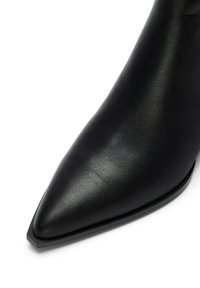 Botín de cuero negro con punta afilada, acabado de alto brillo, textura suave y tacón ancho bajo.