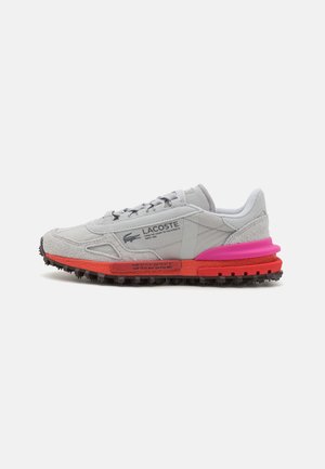 Zapatilla deportiva gris con upper de ante y sintético, acentos en rosa y naranja, suela texturizada y cierre con cordones. Presenta un logotipo impreso.