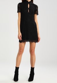 Black lace dress with a high collar, short sleeves, keyhole detail, floral pattern, and scalloped hem. Paired with black ankle boots.