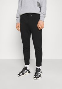Svarta sweatpants med smalnade ben och resårmidja. Matchas med svarta sneakers med vita och grå detaljer. Grå sweatshirt.