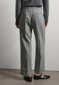 Pantalones de lana grises con pierna ancha, que cuentan con suaves pliegues, un dobladillo vuelto y un bolsillo trasero. Combinados con zapatos negros.