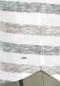 Hvitt T-skjorte med grønne og brune horisontale striper; myk tekstur; har et lite sølvlogo-merke nær bunnen av skjorten.