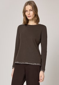 Bruine top met lange mouwen gemaakt van zacht materiaal, met een ronde halslijn en contrasterende dierenprintafwerking bij de manchetten en zoom.