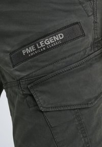 Tmavě zelené cargo kalhoty s kapsou se klopou a černou textilní etiketou s nápisem "PME Legend American Classic" vyšitou nad kapsou.
