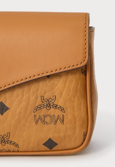 Τσάντα χειρός από καφέ δέρμα με ραμμένο καπάκι και μαύρο τυπωμένο λογότυπο MCM και διαμάντι σχέδιο σε υφασμένη επιφάνεια.