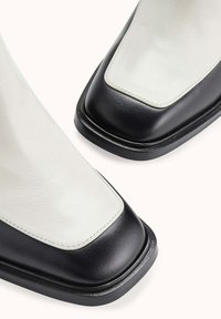 Bottes en cuir à la cheville avec une tige blanche et un embout noir. Forme arrondie avec une texture lisse et une semelle plate noire.