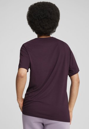 Camiseta corta de manga corta en color granate con un ajuste holgado y cuello redondo. Tejido suave y liso con un ligero brillo, con una costura centrada en la parte posterior.