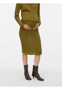 Zelena rebrasta pletena majica za trudnice i suknja u olovku s okruglim izrezom, s kopčanjem na gumb i teksuriranim materijalom. Tamnosmeđe čizme do gležnja.