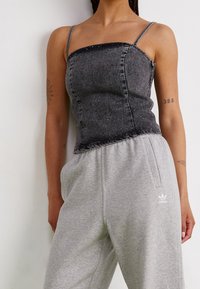 Svart denimcroppad topp med tunna axelband, med en figurnära design och spridda rhinestones. Matchad med grå sweatpants som visar upp en Adidas-logotyp.