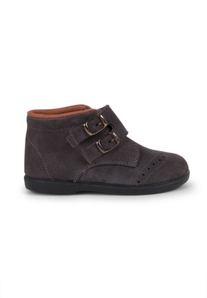 Stivaletto in suede grigio con due fibbie regolabili. Caratterizzato da una punta arrotondata e da una fodera interna marrone a contrasto. Suola piatta in gomma nera.