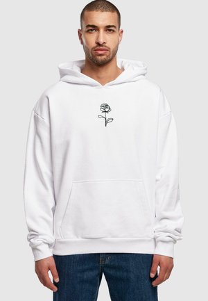 Hvid hættetrøje med en sort linjetegnet rosen grafik på brystet, med en frontlomme og ribbede manchetter. Båret med blå jeans.