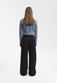 Ljusblå kort denimjacka med ett strukturerat diamantmönster, som matchas med högmidjade svarta vida byxor.