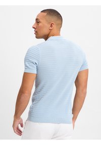 Helles blaues Poloshirt mit kurzen Ärmeln, strukturiertem Muster, geripptem Kragen und Bündchen sowie einer taillierten Passform. Feine Stoffoberfläche.