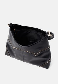 Sac à main en cuir noir à texture lisse, orné de clous dorés et d'un motif en chevrons distinctif sur le devant. Ouverture supérieure avec sangle.