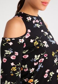 Czarna bluzka w kwiaty z odkrytymi ramionami, z kolorowymi wzorami kwiatowymi w odcieniach różu, żółci i błękitu na teksturowanym materiale.