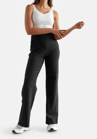 Pantalons larges noirs en tissu doux, dotés d'une taille haute et d'une texture lisse, assortis d'un haut sans manches blanc et de baskets blanches.