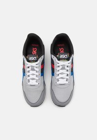 Grå atletiska skor med nätmaterial, med blå och röda accenter, vita snören och svart foder. ASICS-logotypen på tungan.