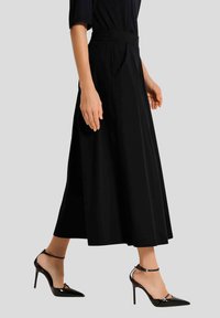 Zwarte wijde rok van gladde stof, met een elastische tailleband en zijplooien. Gecombineerd met glanzende zwarte hoge hakken.