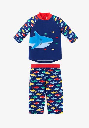 Plavkový tričko s krátkým rukávem s motivem modrého žraloka a červeným límečkem, spárované s plavkami s potiskem barevných žraloků na tmavém pozadí.