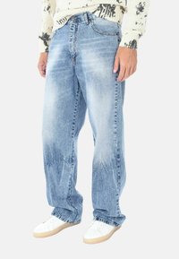 Jeans in denim azzurro chiaro con una vestibilità rilassata. Presentano aree sbiadite, cinque tasche, una patta con bottone e cerniera, e orli leggermente sfrangiati.