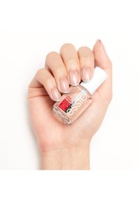 Smalto per unghie in una bottiglia di vetro trasparente con un tappo bianco, tenuto in una mano che mostra una manicure rosa chiaro con punte bianche.