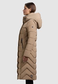 Béžový dlouhý péřový kabát s prošíváním ve vzoru rybí kosti, vysokým límcem, připevněnou kapucí a kapsami na zip po stranách. Hladká, matná textura.