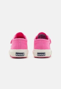 Růžové plátěné tenisky s bílou gumovou podrážkou. Mají texturovaný povrch a branding Superga na patě. Zadní pohled ukazuje polstrovaný límec.