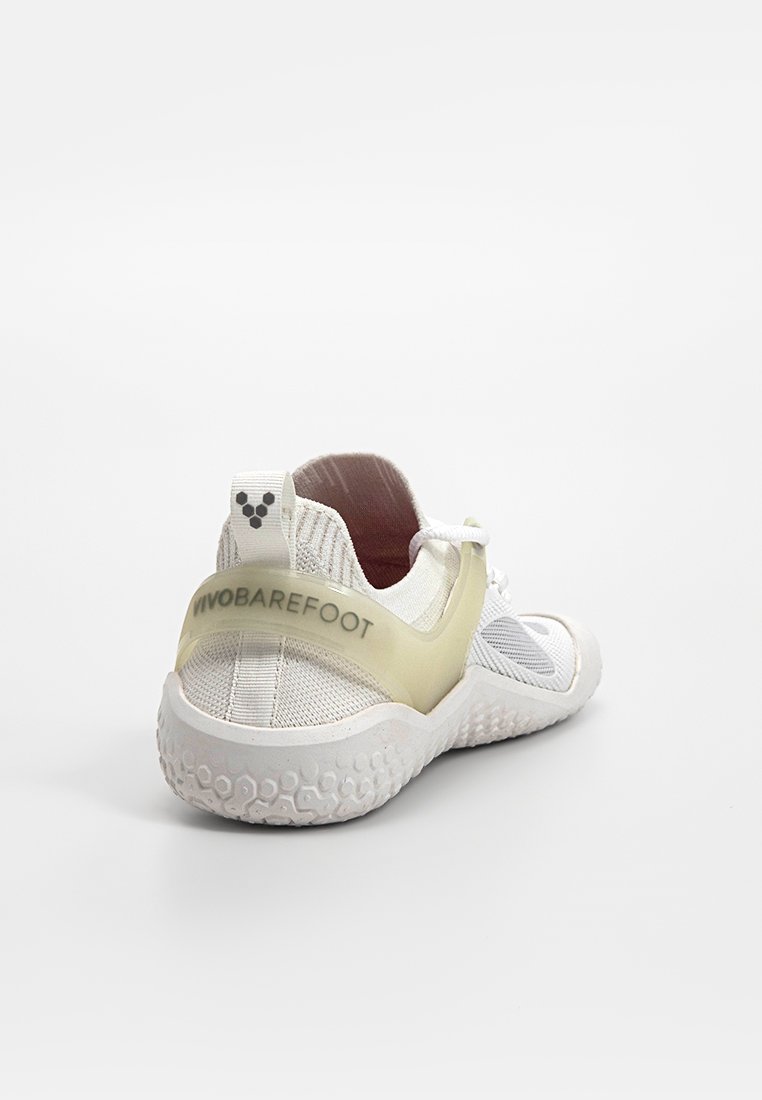 Weißer Sportschuh mit einem atmungsaktiven Mesh-Obermaterial, gelbem Fersenriemen und strukturiertem Gummisohle, der ein minimalistisches Design und eine leichte Konstruktion aufweist.