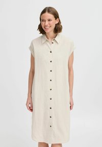 Abito camicia in lino color crema con bottone frontale, maniche corte arrotolate e una vestibilità comoda. Presenta un orlo dritto e una texture sottile.