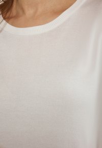Witte t-shirt met korte mouwen en een ronde hals. De stof is glad met een fijne ribbelstructuur. Geen zichtbare patronen of accenten.