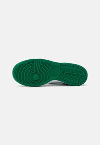Grønn gummisåle på en sneakers med teksturerte gripe mønstre og et sirkulært emblem, som går over i en hvit øverste del.
