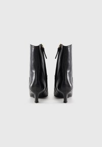 Botas de cano curto em pele preta com bico fino e salto fino. Com fecho de correr lateral com detalhes dourados. Textura lisa.