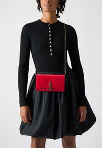 Rød skinncrossbody-veske med rektangulær form, utstyrt med en sølvfarget lås og en kjedeavtak som bæres over en svart ribbet topp.