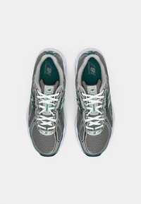 Une paire de chaussures de course New Balance grises et bleu-vert avec des lacets blancs vue de dessus sur un fond blanc.