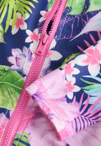 Tissu de maillot de bain à motifs floraux avec des accents roses, une fermeture éclair rose et des feuilles tropicales éclatantes sur un fond bleu marine. Texture douce.