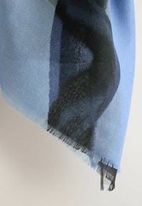 Hele sinine sall tekstuuriga kudumisega, millel on gradientmuster, mis seguneb sügava sinise ja mustaga. Kärpitud ääred lisavad detaili.