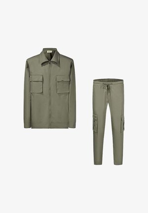 Veste en coton vert olive avec une fermeture éclair à l'avant, un col pointu et deux poches poitrine. Pantalons cargo assortis en vert olive avec des poches latérales et une taille élastique.