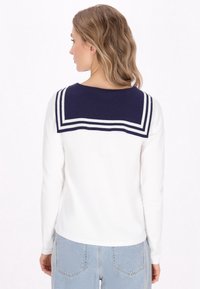 Maglione a maniche lunghe di colore bianco con colletto da marinaio blu navy con righe bianche. Design semplice e aderente, con texture liscia e dettagli minimi.