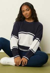 Marinblå och vit randig stickad tröja med ribbad textur, rund halsringning och långa ärmar. Matchas med mörkblå jeans och vita sneakers.