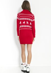 Czerwona dzianinowa sukienka z wysokim kołnierzem, ozdobiona białymi wzorami reniferów i płatków śniegu. Wykończona ściągaczami na mankietach i u dołu.