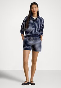 Marineblå og hvitstripet genser med krage og knappedetaljer, kombinert med matchende stripete shorts og svarte flate sko.