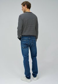 Camisa de manga larga a rayas en blanco y negro combinada con jeans de mezclilla azul, con un corte relajado y diseño clásico de cinco bolsillos.