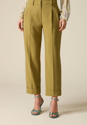 Kalosze w oliwkowo-zielonym kolorze o dopasowanym kroju z mankietami, noszone z niebieskimi, wielopaskowymi sandałami na wysokim obcasie oraz kwiecistą bluzką z długimi rękawami.