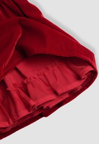 Țesătură de catifea roșie pliată pentru a dezvălui o margine cu volane din plasă roșie stratificată, pe fundal gri.